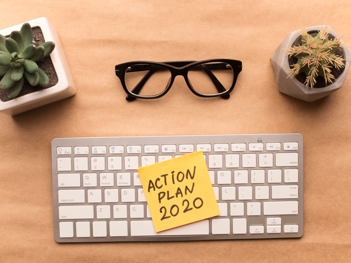 Desk top with keyboard and glasses, post-it on keyboard that says Action Plan 2020